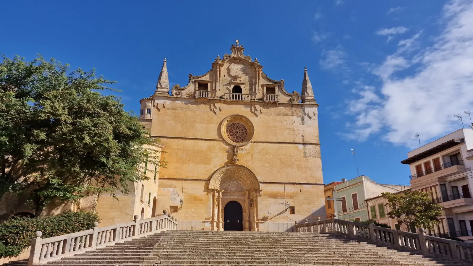The golden marès-stone Baroque facade of Sant Miquel church in Felanitx above its wide stone steps, under a blue sky